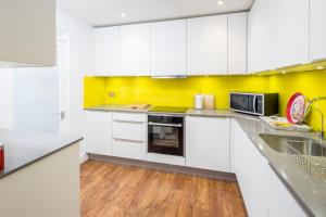 cocina blanca con armarios blancos y microondas en Stunning 2-bed flat w/ garden patio in West London, en Londres