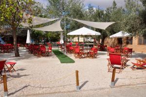 un patio con sillas y mesas rojas y sombrillas blancas en Camping La Estanca, en Alcañiz