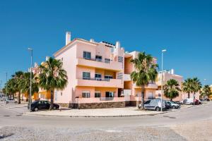 a pink building with palm trees in a parking lot at Formosa Apartment Cabanas Golf in Tavira