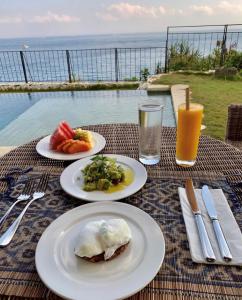three plates of food on a table with a view of the ocean at Villa Tanjung in Nusa Lembongan