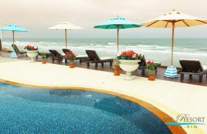 a swimming pool with chairs and umbrellas and the ocean at My resort hua hin A601 in Hua Hin