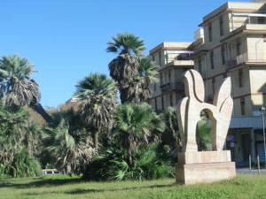 une statue devant un bâtiment planté de palmiers dans l'établissement Ostia Lido Central Rooms, à Lido di Ostia