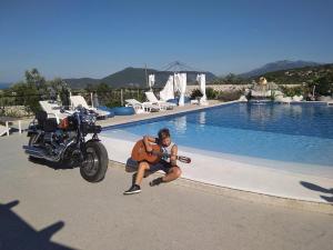 a man holding a guitar next to a motorcycle next to a swimming pool at Luštica Apartments in Lustica