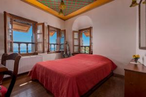 a bedroom with a red bed in a room with windows at Archontiko Melanthi in Makrinitsa