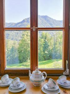 einen Tisch mit Tellern, eine Teekanne und ein Fenster in der Unterkunft Almbauernhof in Ruhpolding