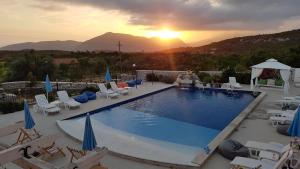 a swimming pool with chairs and umbrellas and the sunset at Luštica Apartments in Lustica