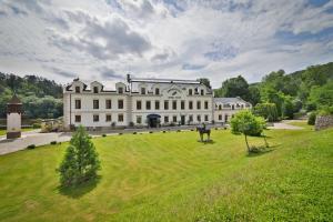 un grand bâtiment blanc sur un champ herbeux dans l'établissement Romantic Hotel Mlýn Karlstejn, à Karlštejn