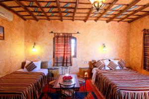 a room with two beds and a table and windows at Riad Nezha in Merzouga