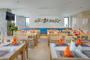 una sala da pranzo con tavoli e sedie con tovaglioli arancioni di Cordial Hotel and Spa a Da Nang