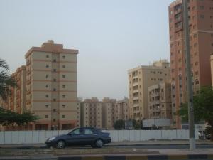 un coche aparcado en un estacionamiento con edificios altos en Red Tower Furnished Apartments, en Kuwait