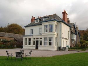 a large white house with chairs in front of it at Muncaster Cottages in Ravenglass