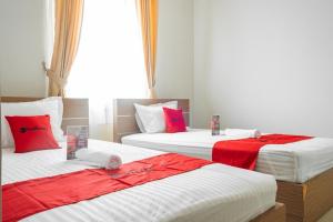 three beds in a room with red and white sheets at RedDoorz near Siloam Karawaci 3 in Tangerang