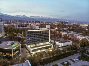 Blick auf eine Stadt mit Gebäuden und Bergen in der Unterkunft Novotel Almaty City Center in Almaty