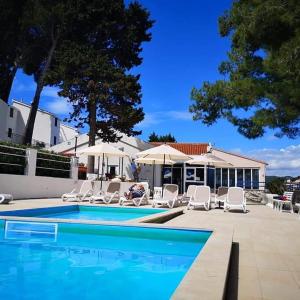 a swimming pool with white chairs and umbrellas at Lumbarda Driftwood in Lumbarda