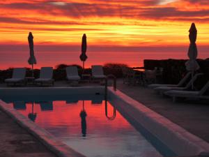 - une piscine avec des chaises et des parasols au coucher du soleil dans l'établissement Lithia Villas, à Folégandros