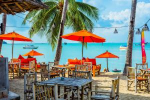 a beach with tables and chairs and the ocean at Secret Garden Beach Resort in Bangrak Beach