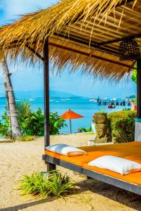 a bed under a straw umbrella on a beach at Secret Garden Beach Resort in Bangrak Beach