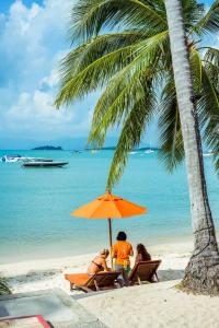 three people sitting under an orange umbrella on the beach at Secret Garden Beach Resort in Bangrak Beach