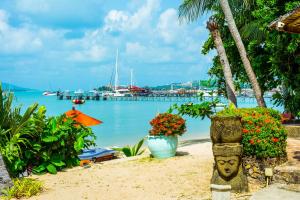 a beach with flowers and a harbor with boats at Secret Garden Beach Resort in Bangrak Beach