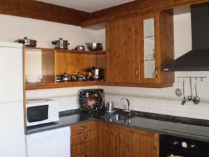 cocina con armarios de madera, fregadero y microondas en Casa Rural Las Tuyas en Segovia en Palazuelos de Eresma