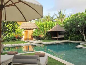 a swimming pool with an umbrella next to a house at Nyaman Villas in Seminyak