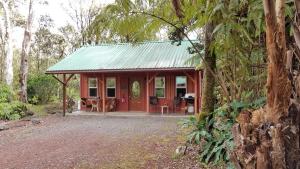 uma cabana vermelha com um telhado verde na floresta em Alii Kane Cottages with Loft em Volcano