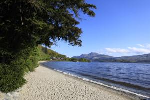 a beach with trees and water and mountains in the background at Fab-u-Luss in Luss