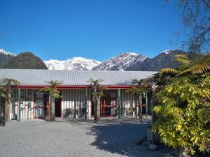 a building with palm trees in front of mountains at Glow Worm Accommodation in Franz Josef