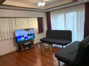 ein Wohnzimmer mit einem TV, einem Sofa und einem Stuhl in der Unterkunft ガナダン中央駅 1f 無料駐車場 in Kagoshima