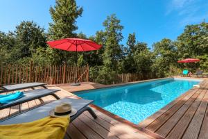 a swimming pool with a wooden deck and a red umbrella at Villa Nakalta in CazoulÃ¨s