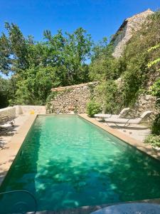 une piscine d'eau bleue en face d'un mur en pierre dans l'établissement La Magnanerie d'Audabiac, à Lussan