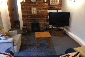 een woonkamer met een televisie en een stenen open haard bij Rose Cottage in Ludham