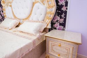 uma cama com uma cabeceira dourada e branca ao lado de uma mesa lateral em Razmestim в ЖК Шахристан на 15 этаже em Almaty