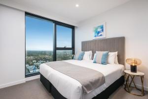 a bedroom with a large bed and large windows at Sky One Apartments by CLLIX in Box Hill