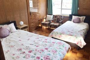 a bedroom with two beds and a chair and a window at SMILE ONE GUEST HOUSE OKINAWA in Yomitan