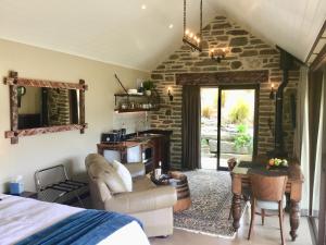 a bedroom with a bed and a table and a room with a stone wall at Hawkridge Chalet - Honeymooners Chalet in Arrowtown