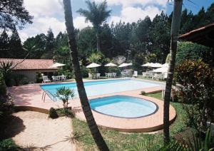 una piscina en un patio con sillas y sombrillas en Estalagem Fazenda Lazer, en Carandaí
