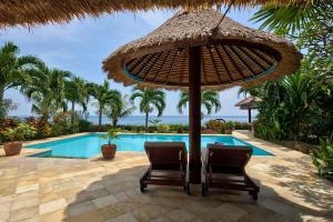 duas cadeiras debaixo de um guarda-sol ao lado de uma piscina em Villa Cahaya - Bali Sea Villas Beachfront and private pool em Pengastulan