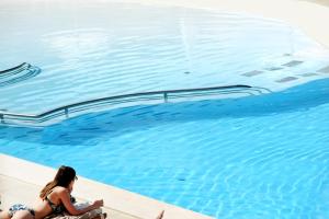 a woman in a bikini sitting next to a swimming pool at Le Calette Bay in Cefalù