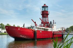 una barca rossa e bianca in acqua con un faro di Lightship Amsterdam ad Amsterdam