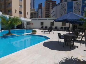 uma piscina com mesas e cadeiras e um guarda-sol em Hotel Geranium em Balneário Camboriú
