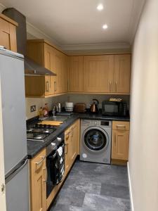 uma cozinha com armários de madeira e uma máquina de lavar e secar roupa em Dunfermline GF flat, 5 min walk to Train St. and High St. em Dunfermline