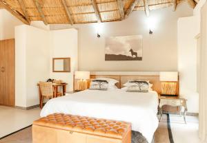 a bedroom with a large white bed and a bench at Tambuti Lodge in Pilanesberg