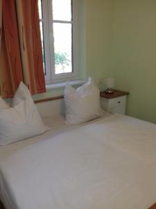 een wit bed met kussens in een kamer met een raam bij Ferienwohnung Waren (Müritz) - Haus Buchen am Tiefwarensee - 3 Zi in Waren