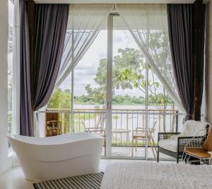 een badkamer met een bad voor een groot raam bij White Wall Riverfront Hotel in Kamphaeng Phet