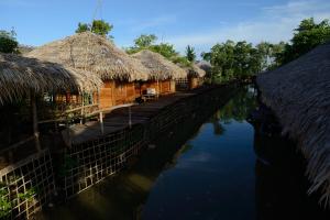 a row of houses with thatched roofs next to a river at Baan​ Tonlamphu​ Pakpra in Phatthalung