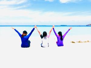 drie mensen zitten op het strand met hun handen in de lucht bij Maafushi View in Maafushi