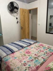 a bedroom with a bed with a flower blanket and a fan at Apartamento de 2 quartos com Ar Condicionado na Enseada in Guarujá