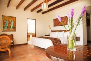 um quarto com uma cama e um vaso com flores roxas numa mesa em La Hacienda Bahia Paracas em Paracas