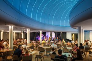 una multitud de personas sentadas en mesas en una habitación con un escenario en Los Zocos Impressive Lanzarote, en Costa Teguise